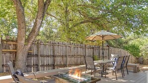 An outdoor patio with a fire pit, seating, and a wooden fence. - Revins Haus - Fire Pit & Walk to Main St (Fredericksburg)