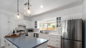 A modern kitchen with white cabinetry, a stainless steel refrigerator, and pendant lighting. - Revins Haus - Fire Pit & Walk to Main St (Fredericksburg)