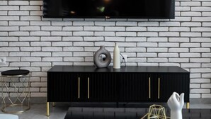 A modern living room with a white brick wall, a black entertainment unit, and a flat-screen TV mounted above it displaying the Netflix logo. - Mythic Meteora (ΚΑΛΑΜΠΑΚΑ)