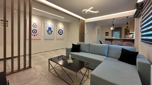 A modern living room with a sectional sofa, a glass coffee table, and abstract wall art. - Mythic Meteora (ΚΑΛΑΜΠΑΚΑ)