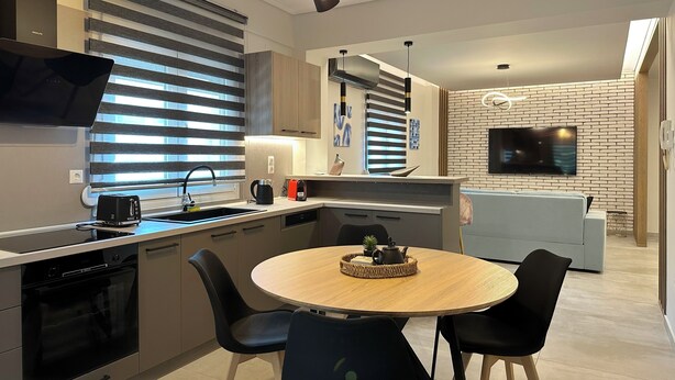 A modern kitchen with a dining area, a built-in oven, and a flat-screen TV. - Mythic Meteora (ΚΑΛΑΜΠΑΚΑ)
