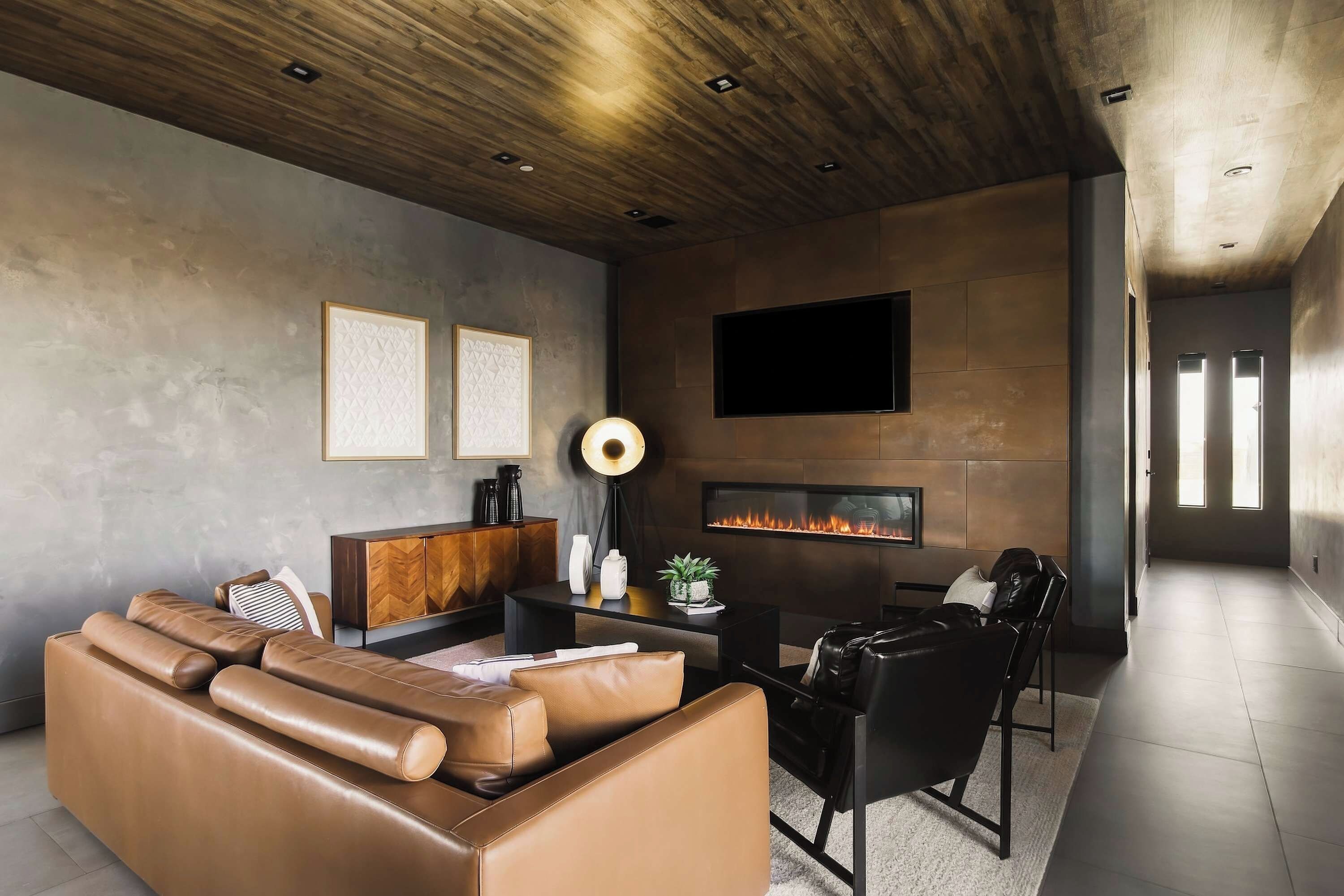 A modern living room with a leather sofa, a coffee table, a fireplace, and a flat-screen TV mounted on the wall.