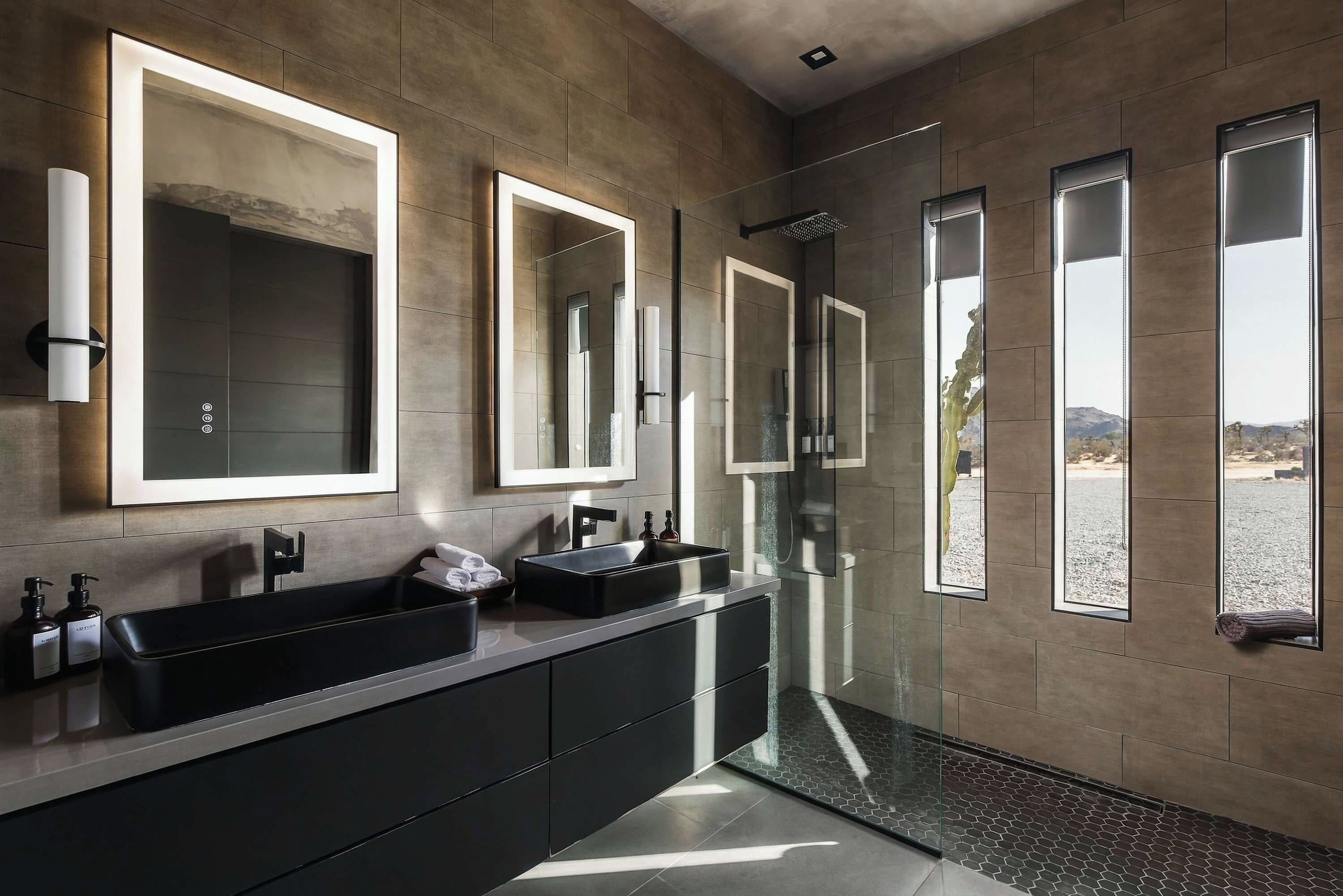 Un baño moderno con un espejo grande, un lavamanos negro y una cabina de ducha de vidrio.