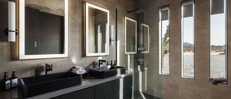 Un baño moderno con un espejo grande, un lavamanos negro y una cabina de ducha de vidrio.