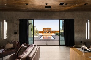 Un interior moderno con un sofá de cuero, una mesita de madera y vistas a una zona de piscina exterior.