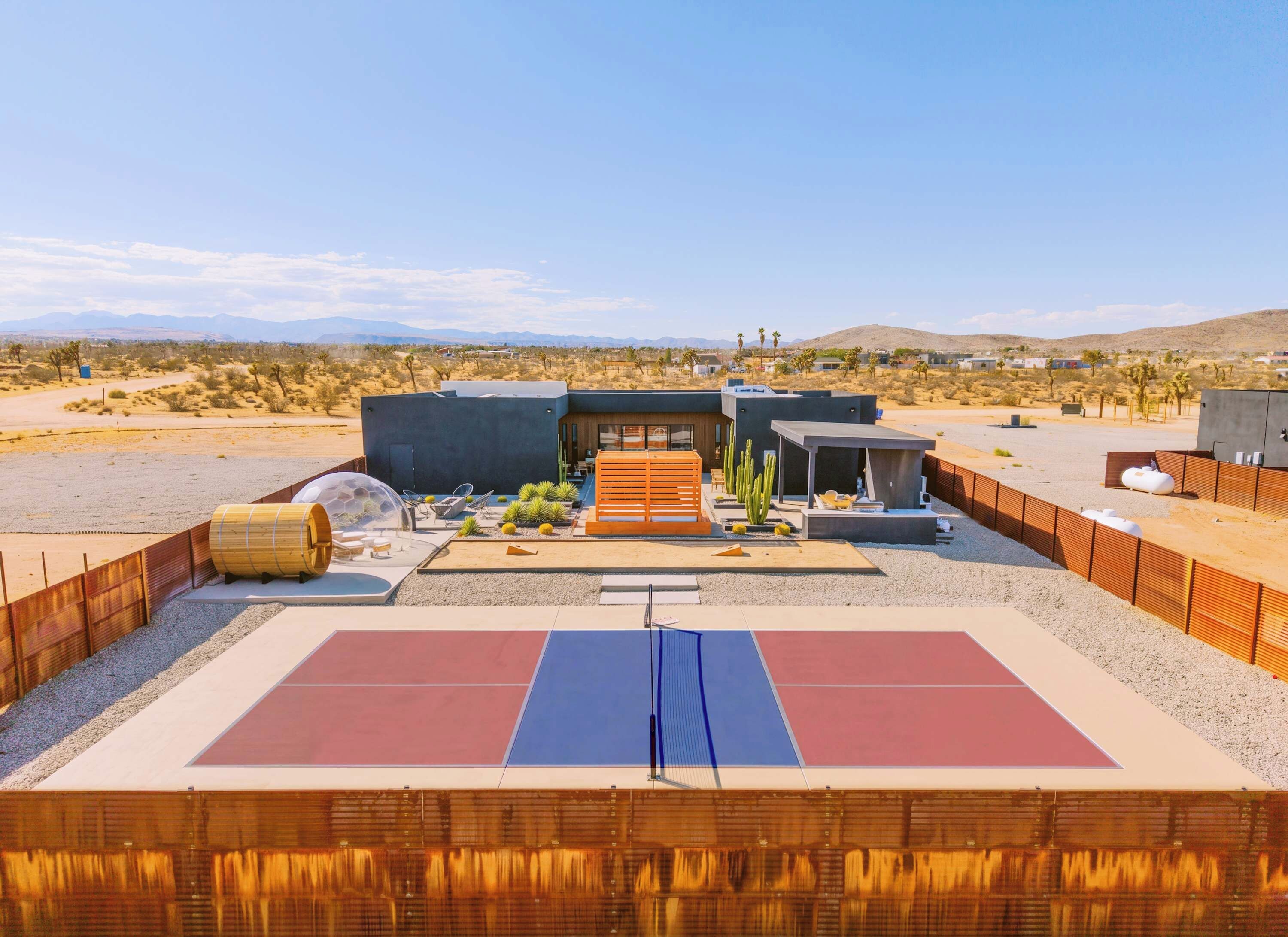 A modern outdoor tennis court with a wooden fence, a wooden pergola, and cacti.