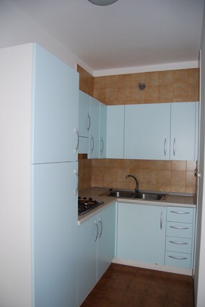 Een kleine keuken met lichtblauwe kastjes, een roestvrijstalen spoelbak en een betegelde achterwand.