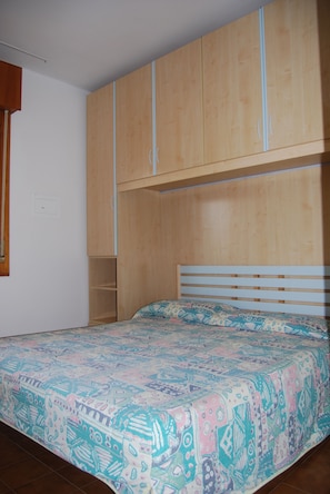 Een slaapkamer met een bed, een houten garderobe en een raam.