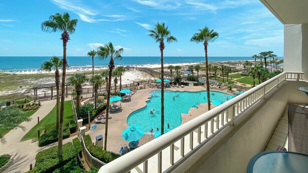 Zona de piscina con palmeras, vista a la playa y cielo despejado.