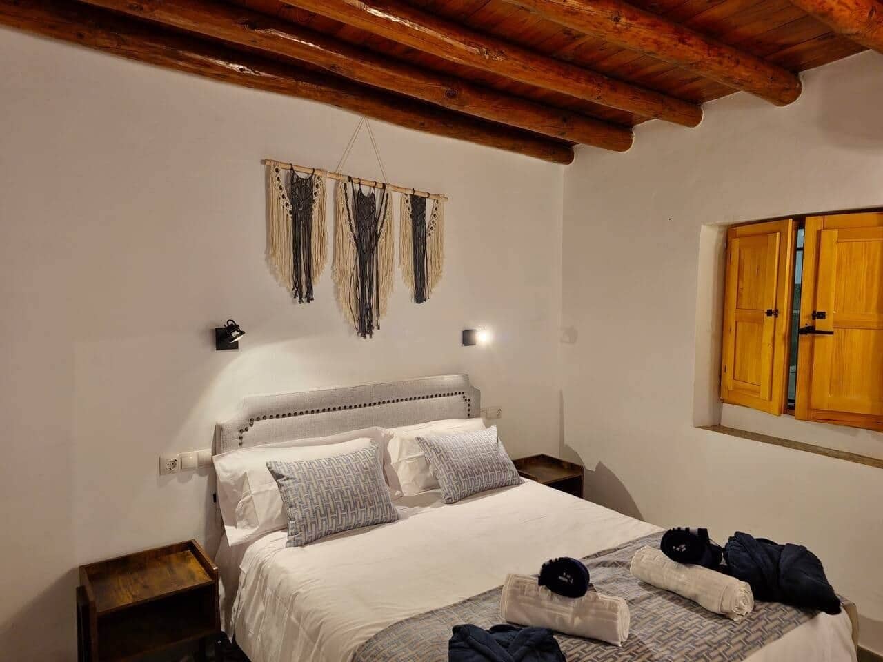 Un dormitorio con cama, mesitas de noche, luz empotrada en la pared, techo de madera y armario de madera.