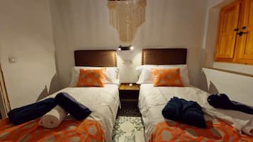 Een kamer met twee bedden, elk voorzien van een hoofdeinde, een hangende macramé decoratie en een houten garderobe.