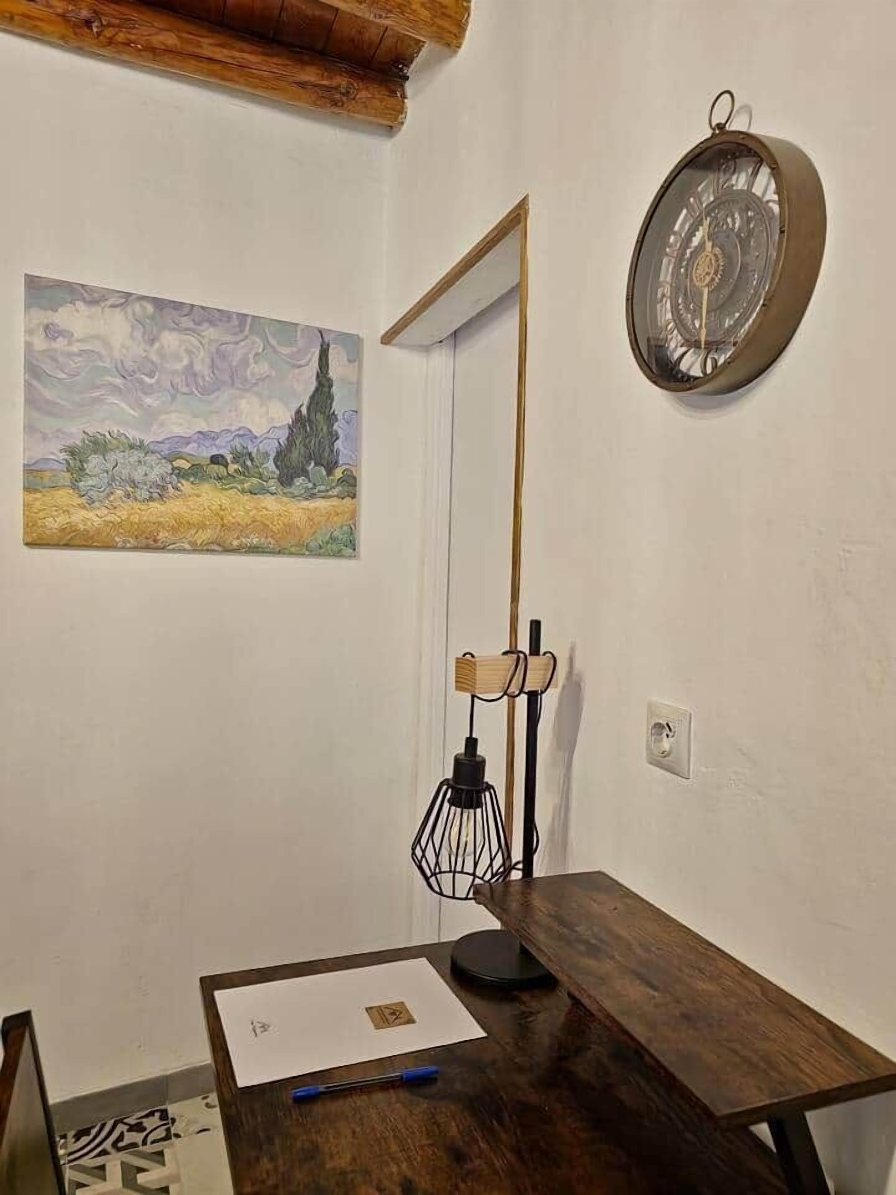 Une pièce avec un bureau en bois, un tableau, une horloge murale et un miroir.