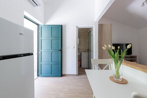 Une cuisine moderne avec une porte de couleur turquoise, un réfrigérateur blanc et un coin repas agrémenté d’un vase en verre rempli de fleurs.