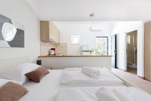 Une chambre d’hôtel moderne équipée d’un lit, d’une petite kitchenette et d’une salle de bain visible à travers une porte ouverte.