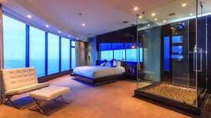 A modern hotel room with a large bed, a seating area, and a glass-enclosed shower.