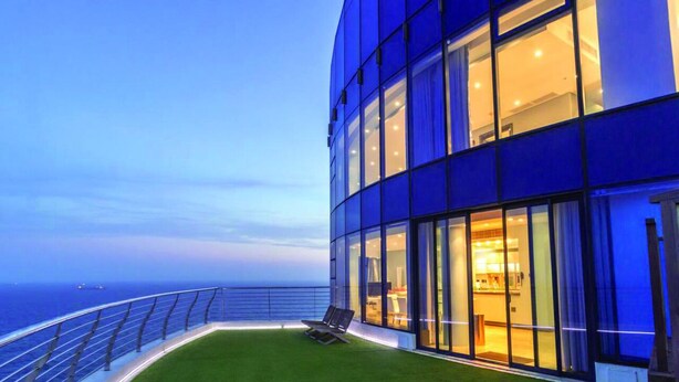 A modern building with large glass windows, a grassy deck, and a railing overlooking the ocean.