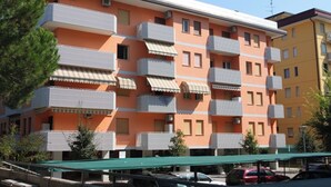 A multi-story residential building with balconies, a green awning, and parked cars.