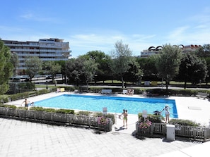 Piscina cercada por grade, bancos e árvores.