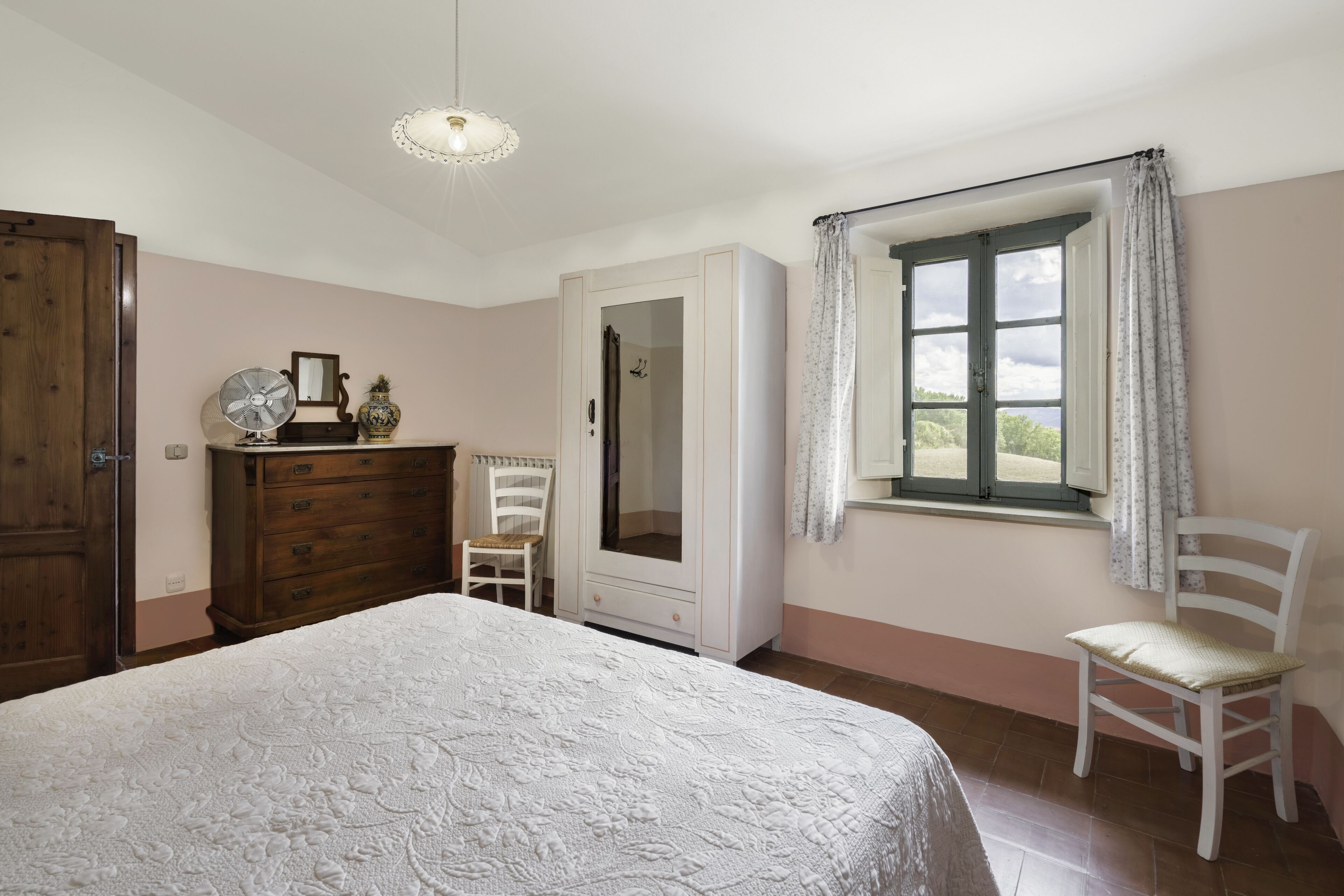 Une chambre à coucher avec un lit, une commode, un miroir et une fenêtre avec des rideaux.