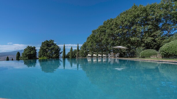 A clear blue pool with lounge chairs and umbrellas, surrounded by trees and a stone wall. - Orcia Panoramic View With Pool (Sarteano)