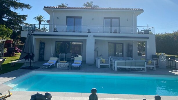 Ett tvåvåningshus med en swimmingpool, utomhusmöbler och en balkong.