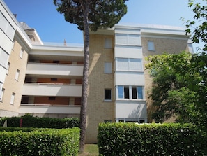Un immeuble résidentiel à plusieurs étages, doté de balcons, d’une façade en briques et d’une haie bien entretenue.