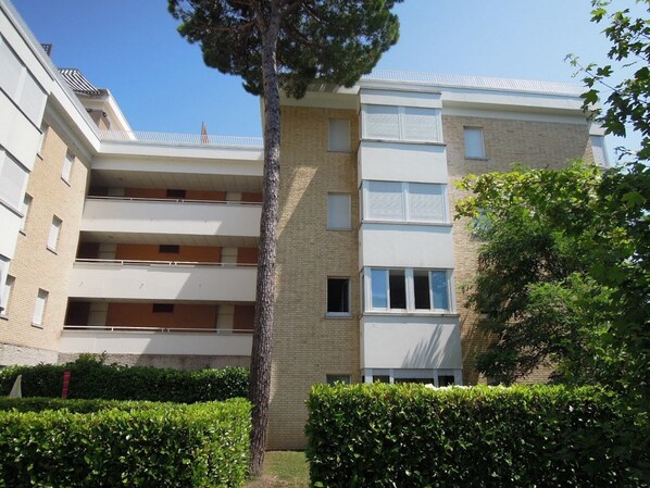 A multi-story residential building with balconies, a brick facade, and a well-maintained hedge. - Comfortable Apartment With Parking in Bibione (San Michele al Tagliamento)