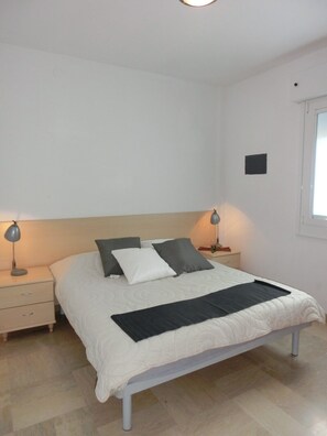 Une chambre à coucher comprenant un lit, deux tables de chevet, une commode, une fenêtre et un luminaire fixé au mur.