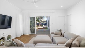 A modern living room with a flat-screen TV, a sofa, and a dining area with a table and chairs.