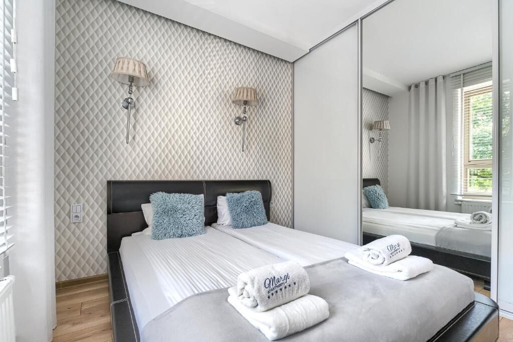 A modern bedroom with a large bed, two wall-mounted lamps, and a large mirror reflecting the room.