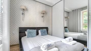 A modern bedroom with a large bed, two wall-mounted lamps, and a large mirror reflecting the room.