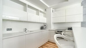 A modern kitchen with white cabinetry, a wooden floor, and a built-in stove. - MARGI Eclipse Apartament (Szczecin)