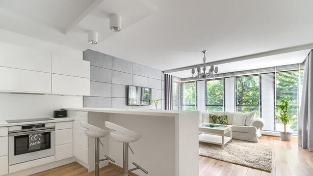 A modern kitchen with white cabinets, a built-in oven, and two bar stools. - MARGI Eclipse Apartament (Szczecin)