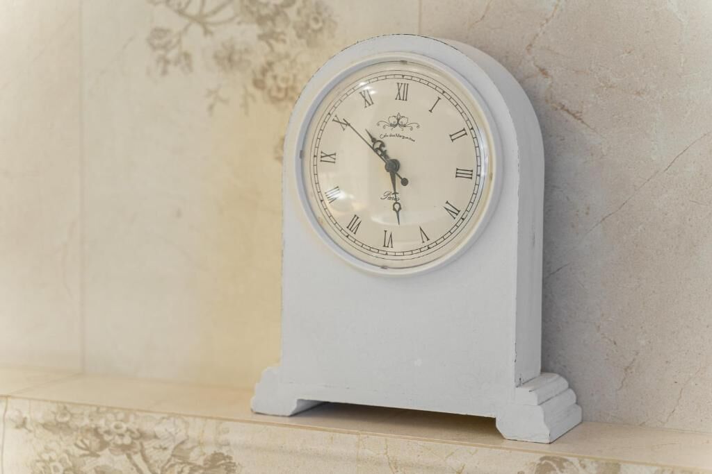 Eine weiße Wanduhr mit römischen Ziffern und floralem Dekor, an einer Wand befestigt.