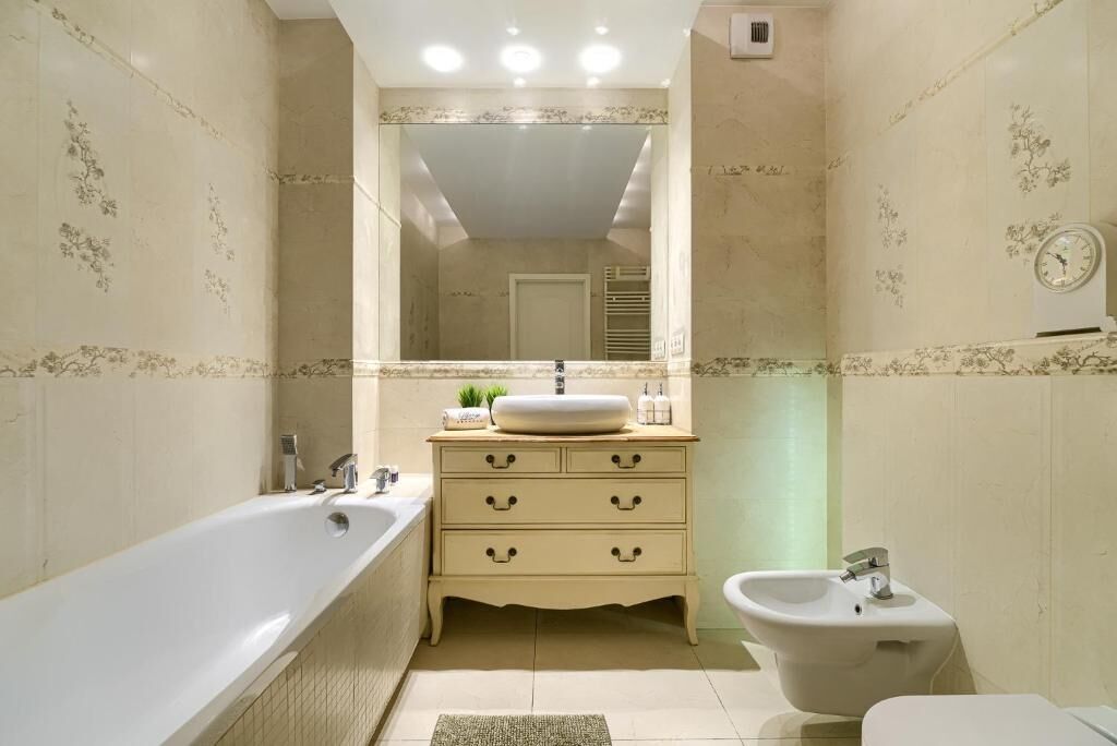 A bathroom with a bathtub, a sink, a vanity with drawers, a mirror, and a wall clock.