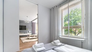 A modern bedroom with a large bed, a view of the outdoors through a window, and a separate bathroom area visible through a mirror. - MARGI Eclipse Apartament (Szczecin)