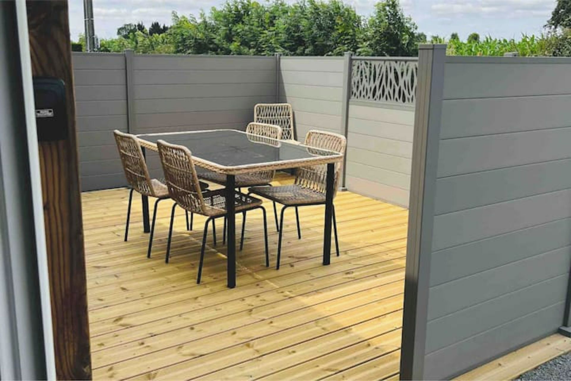 A wooden deck with a table and chairs, enclosed by a grey fence with decorative lattice panels.