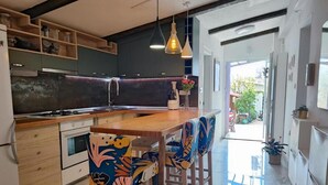 A modern kitchen with a central island, wooden chairs with colorful upholstery, and pendant lighting. - Marijano Dvosobni Apartman s Vrtom (Zadar)