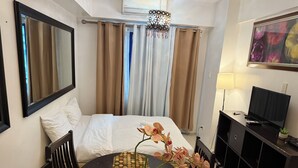 A hotel room with a bed, a dining table with chairs, a TV, and a painting on the wall. - 2BR Poolview  for 6-10 pax at Sea Residences Mall of Asia 402403 (Pasay)