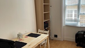 A room with a wooden table, a chair, a bookshelf, and a window with blinds. - SOOTHEUS - SOHO7 (London)