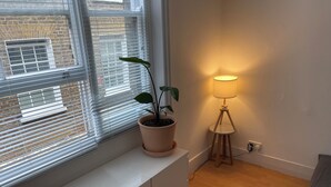 A room with a window, a potted plant, a lamp, and a bench. - SOOTHEUS - SOHO7 (London)