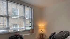 A room with a bed, a desk, a window with blinds, a potted plant, and a lamp. - SOOTHEUS - SOHO7 (London)