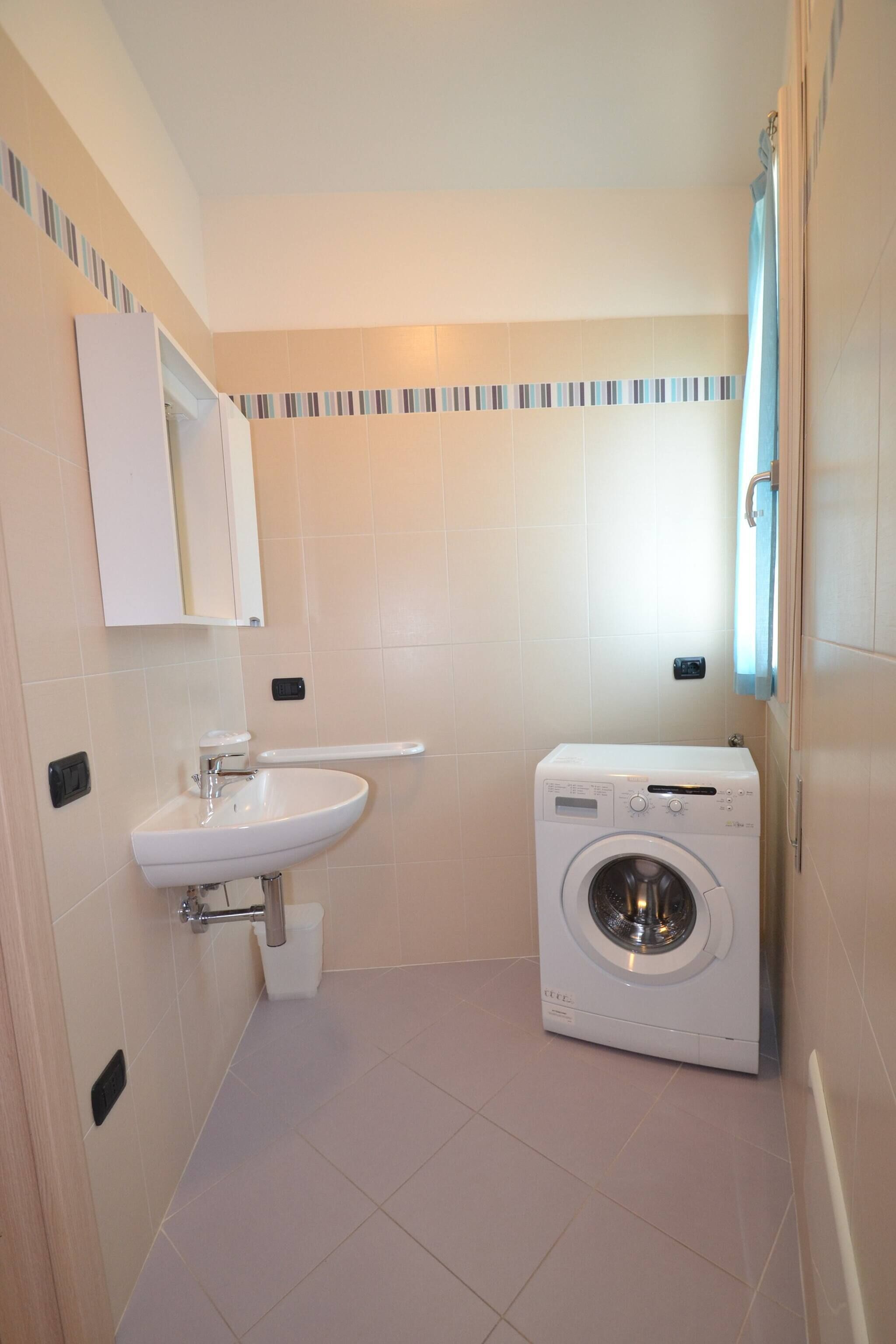 Une petite salle de bain propre, équipée d’un lavabo, d’un miroir et d’un lave-linge.