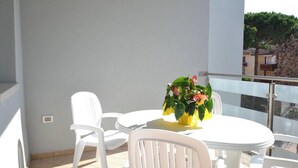 A balcony with a white table and chairs, a potted plant, and a view of buildings and trees. - Modern Flat in Central Location (Rosolina)