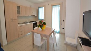 A modern kitchen with light wooden cabinets, a dining table with chairs, and a TV on the right. - Modern Flat in Central Location (Rosolina)
