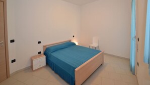 A bedroom with a bed, bedside table, chair, and a door. - Modern Flat in Central Location (Rosolina)