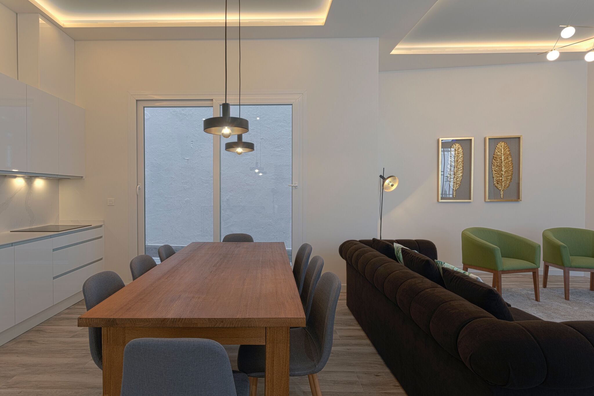 A modern living room with a wooden dining table, a brown sofa, and green chairs.