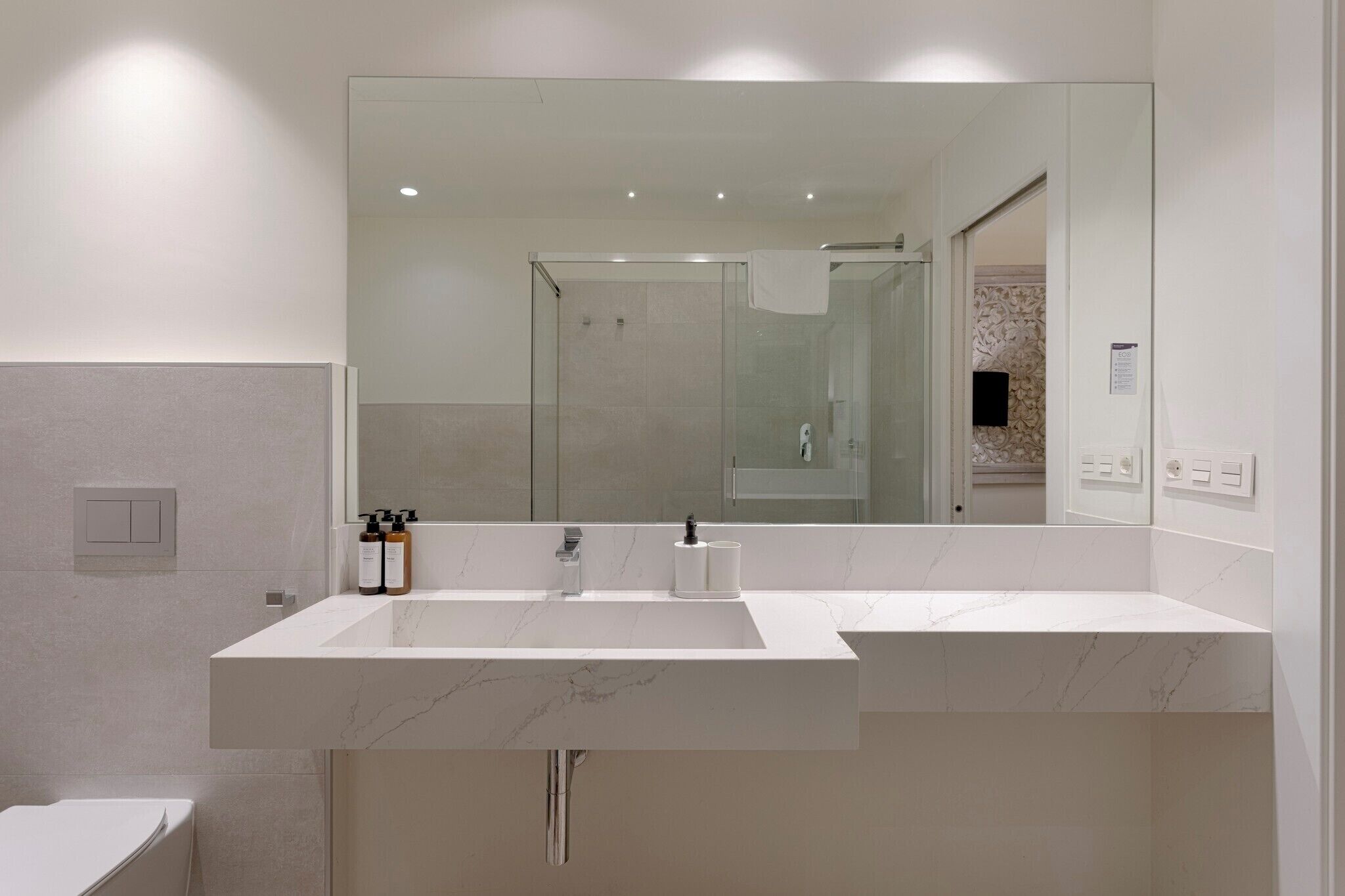 A modern bathroom with a large mirror, a white sink, and a glass shower enclosure.