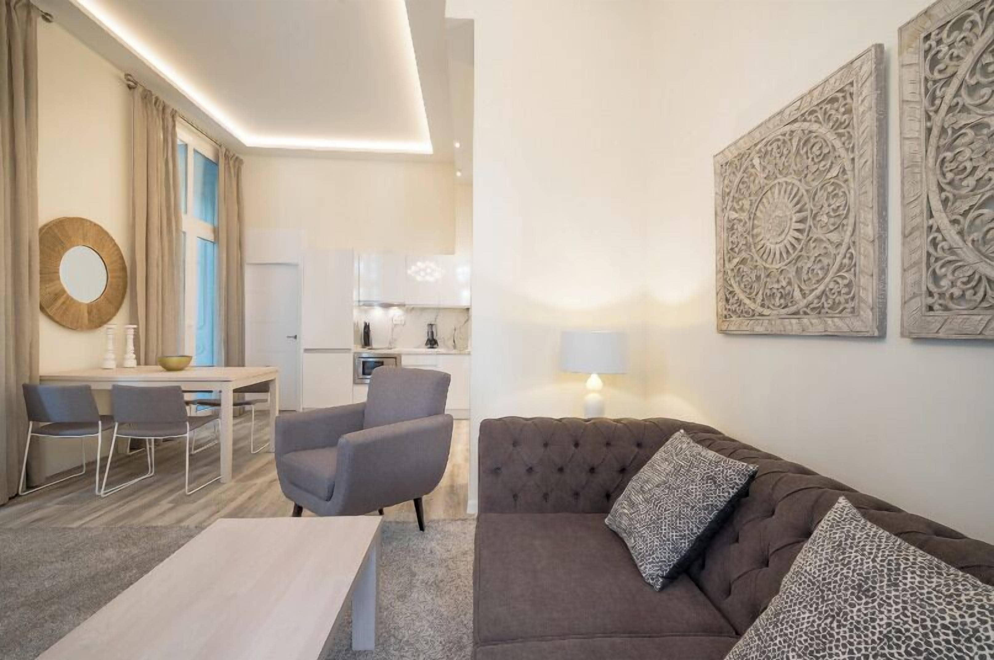 A modern living room with a sofa, chairs, a dining table, and a kitchen in the background.