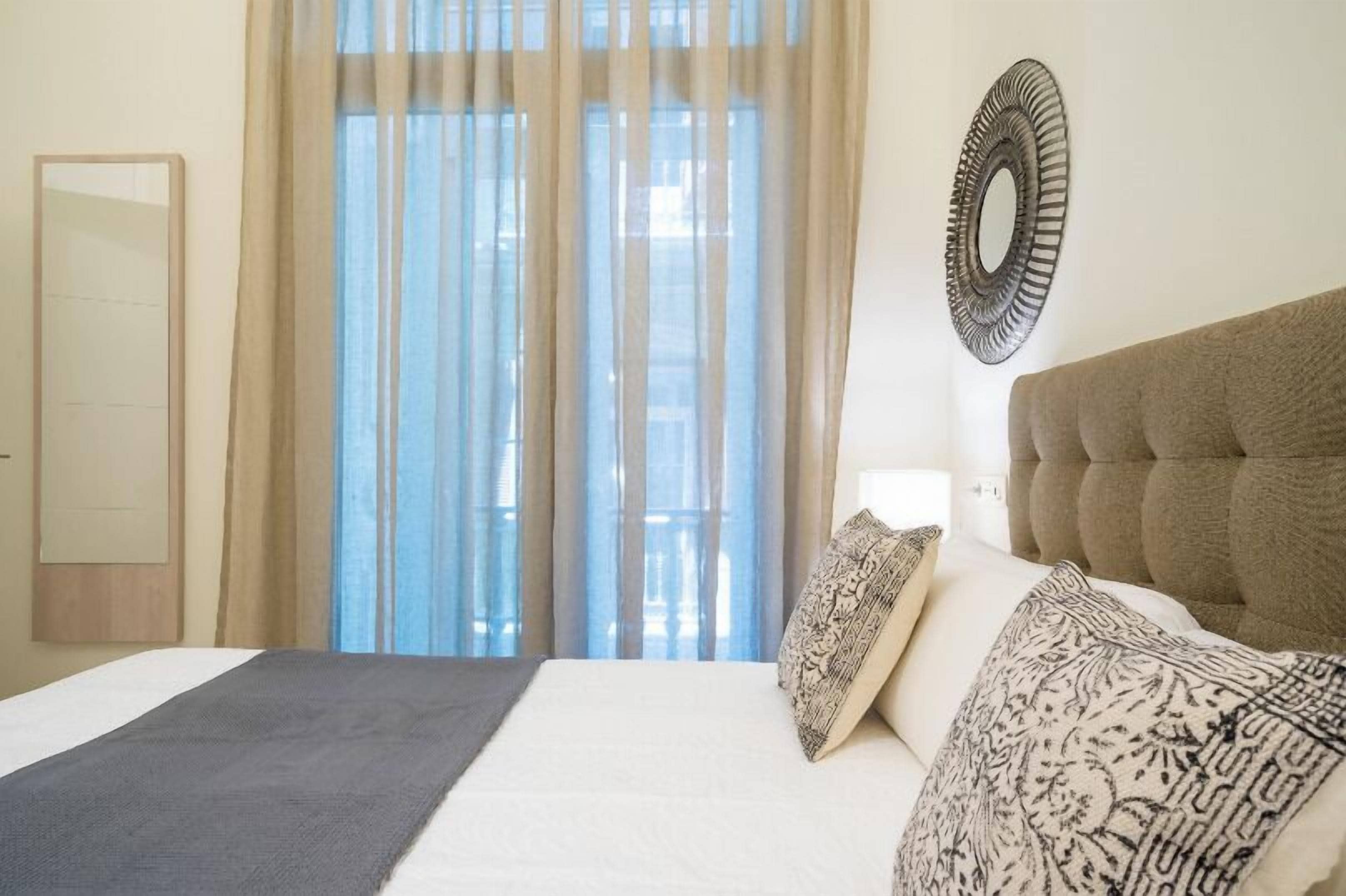 Ein Schlafzimmer mit einem großen Bett, einem Spiegel und einem Fenster mit durchsichtigen Vorhängen.